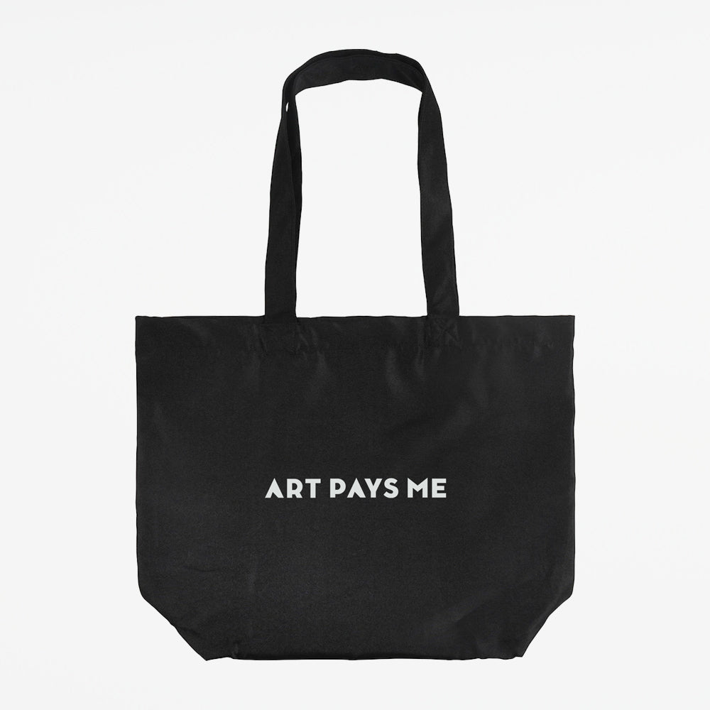 Black cotton tote bag with Art Pays Me printed on it.