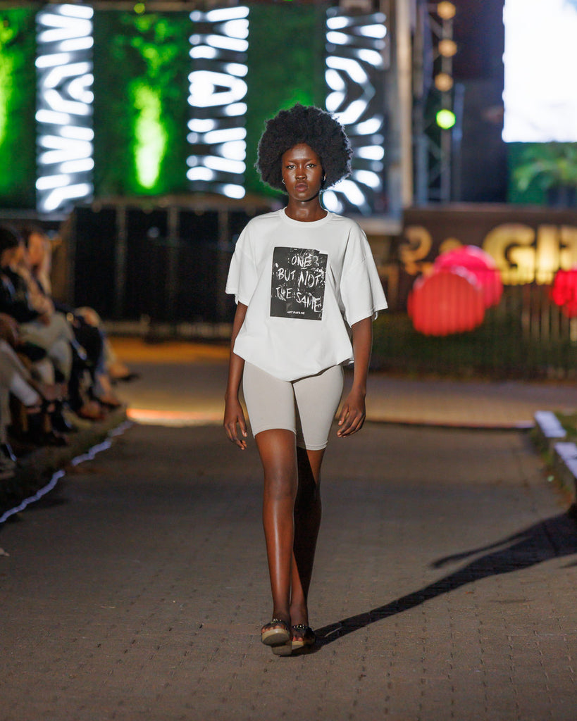 A young Black woman walks a fashion runway wearing a white t-shirt