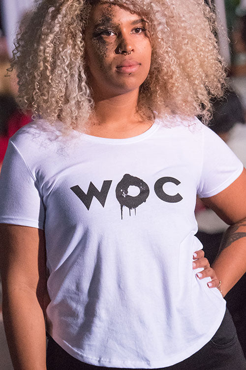 A light skinned Black woman with curly hair wearing a white t-shirt with a scooped bottom. 