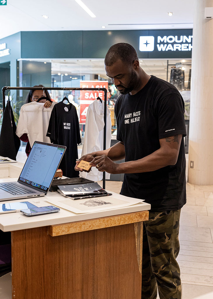 Duane wearing the black Many Faces One Halifax Tee at Halifax Shopping Centre during an Art Pays Me and HaliTube pop-up event. 