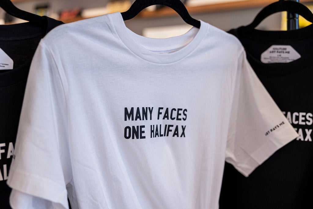 Many Faces One Halifax Tee, White on a hanger at Halifax Shopping Centre. Photo by Emma Lomas.